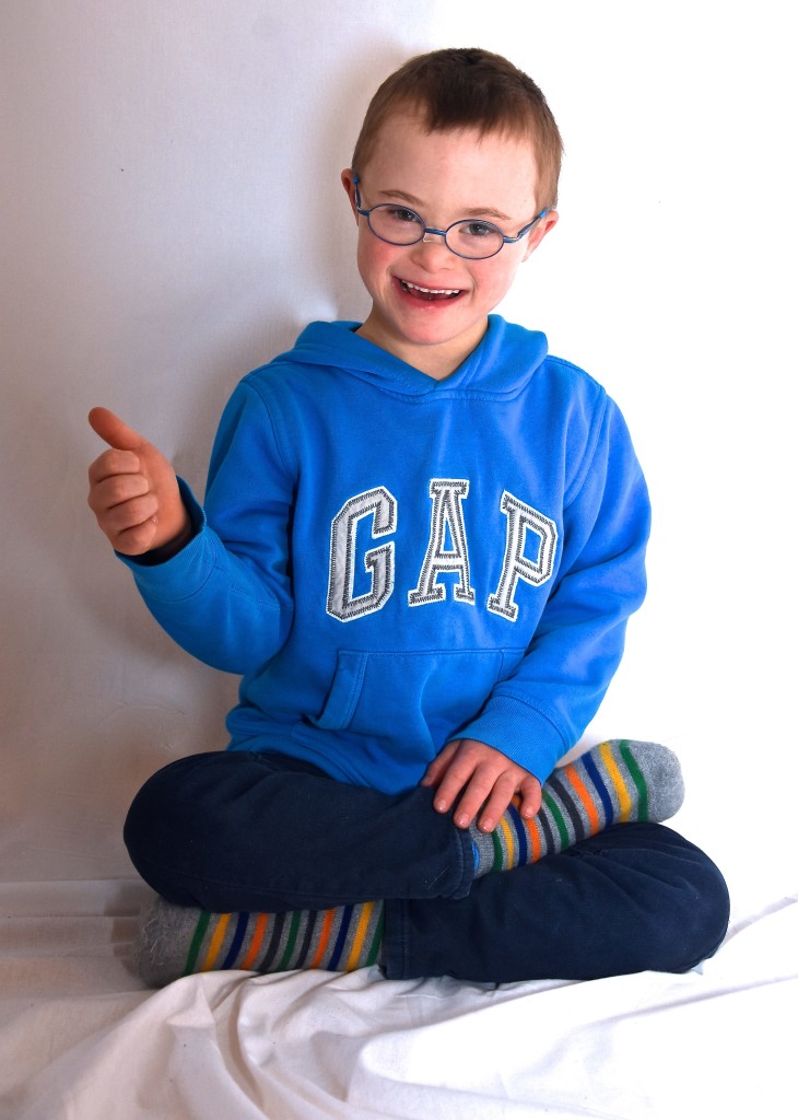 Ein Junge mit einem blauen Pullover sitzt im Schneidersitz und zeigt den Daumen hoch