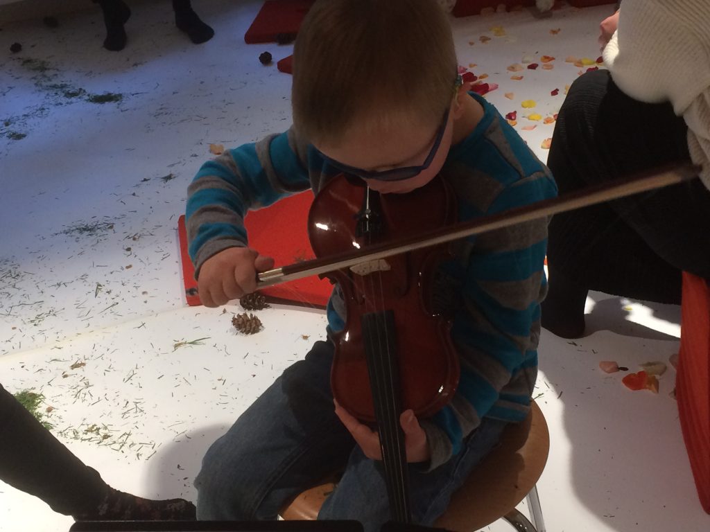 ein Junge kniet mit einer Geige auf dem Fußboden