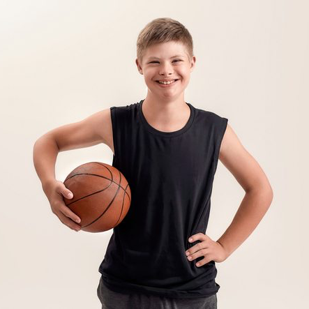 Ein sportlicher Junge mit dunkelblondem kurzen Haar schaut lächelnd in die Kamera. Er ist ungefähr 13 Jahre alt und trägt ein schwarzes ärmelloses Sportshirt. Die linke Hand ist locker in die Hüfte gestemmt und in der rechten Hand hält er einen Basketball an die Seite seines Oberkörpers.